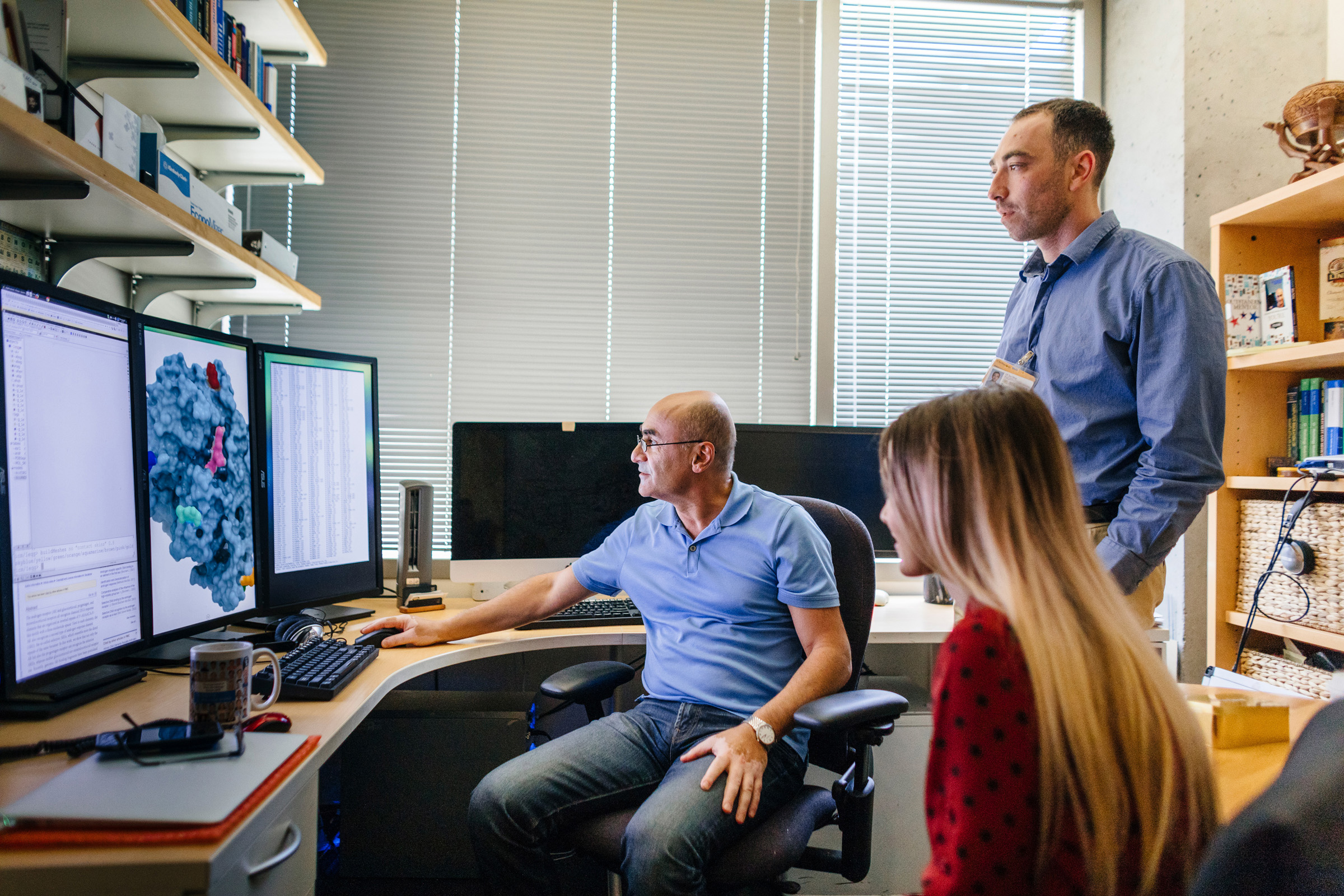 three researchers looking at three computer monitors reviewing data