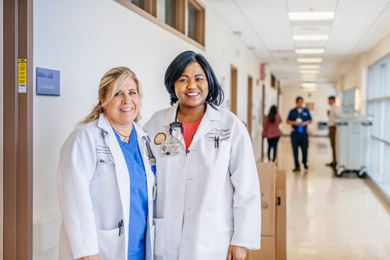 two physicians standing next to each other in hospital corridor smiling