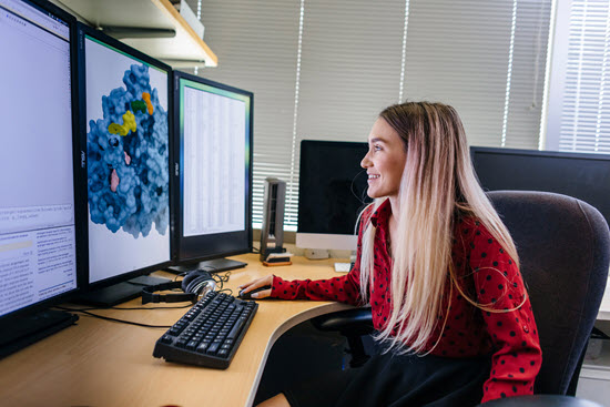 woman sits in front of three large computer monitors reviewing data