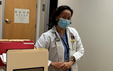 dr. amy leu with mask and white lab coat in a doctors office